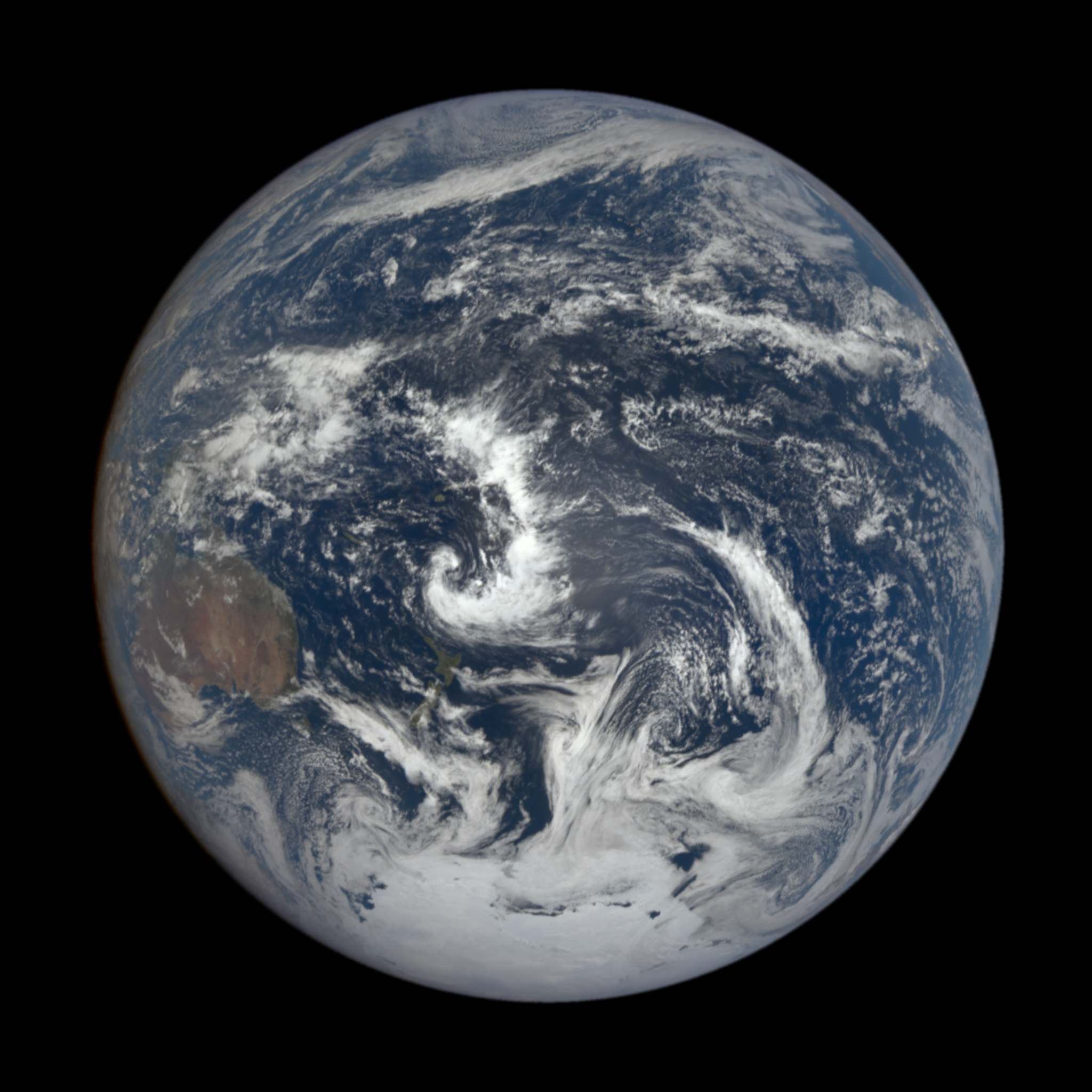 The whole Earth photographed from the DSCOVR satellite a million miles out — the Pacific Ocean, swirling white cloud systems, Australia rust-red at the left edge, Antarctica white at the bottom, against black space.