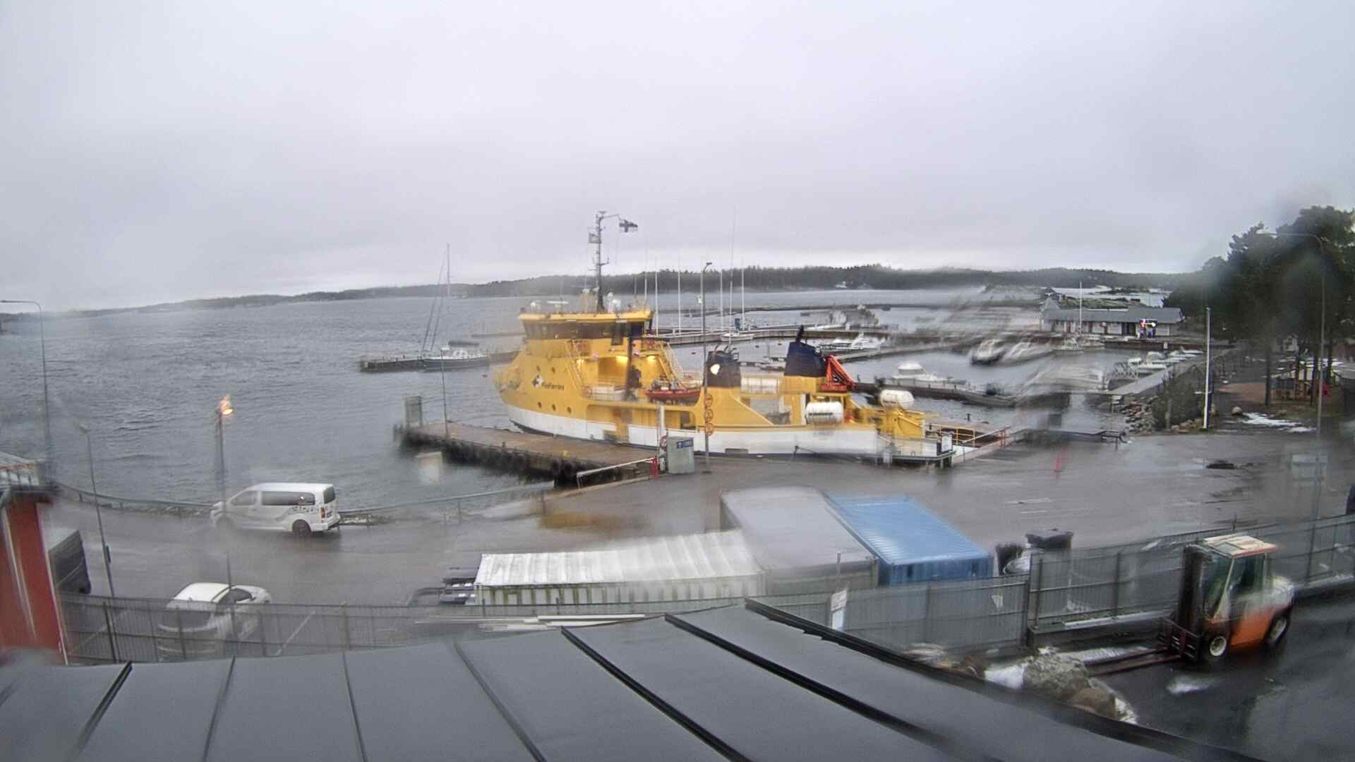 A Finnish ferry terminal under grey sky — a bright yellow ferry at the dock, forested islands behind, seen through a rain-spotted window.