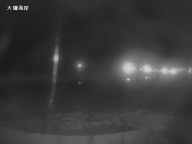 A dark, foggy seafront at Ōiso, Japan — streetlights diffusing into mist, grainy night, the Japanese label 大磯海岸 in the corner.